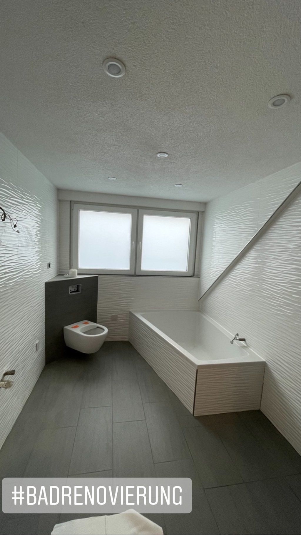 Renoviertes Badezimmer mit hellen, strukturierten Wänden, Wanne und dunklem Boden.