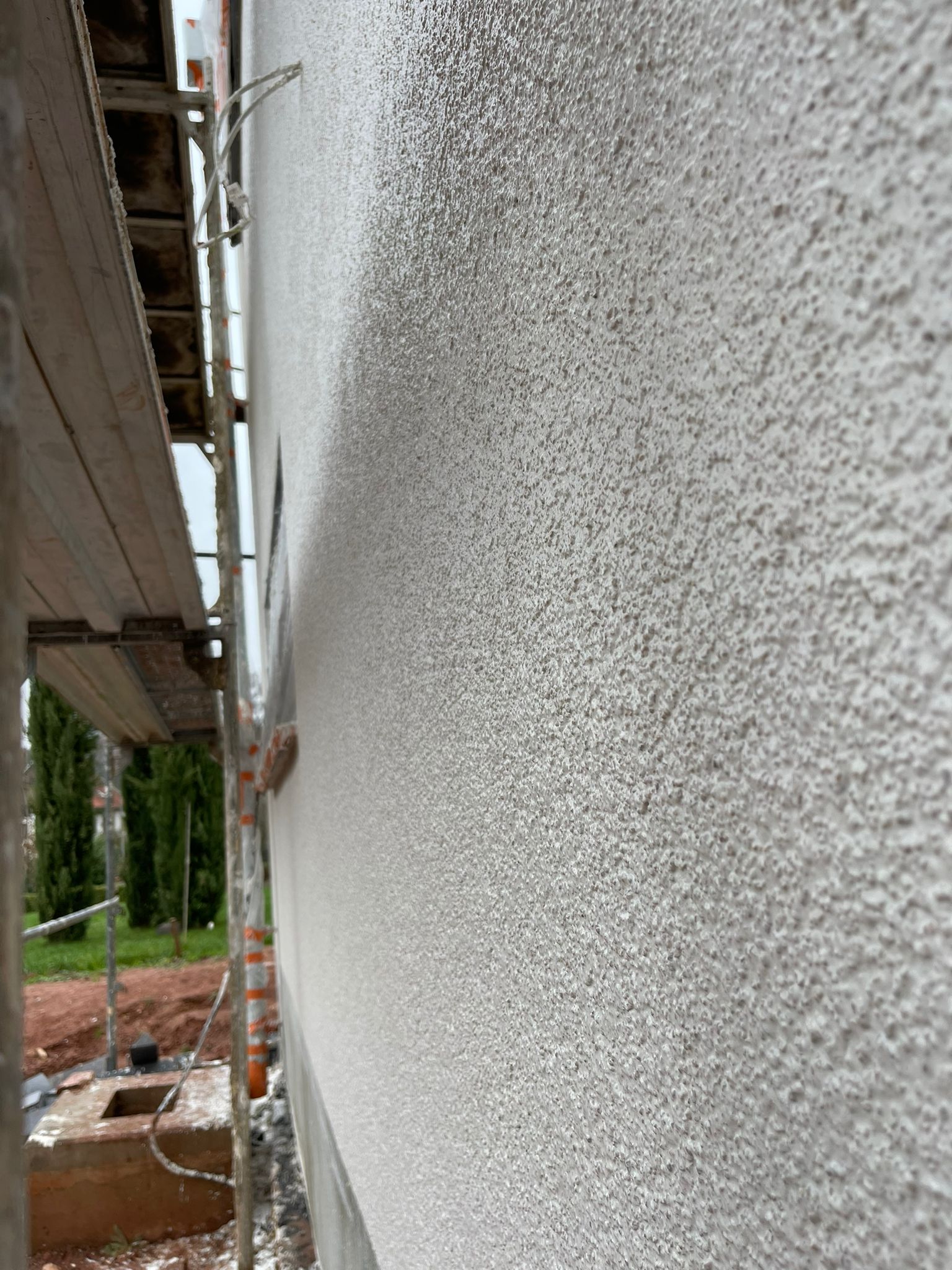 Nahaufnahme einer frisch verputzten Fassade mit gleichmäßiger Körnung, links das Baugerüst.
