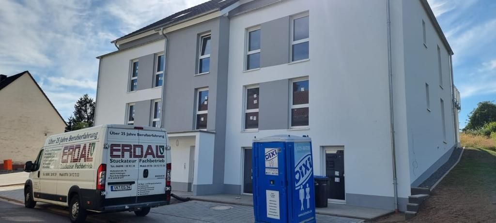 Frisch verputztes Mehrfamilienhaus mit grauen Fensterbändern, davor der Firmenwagen von Erdal.