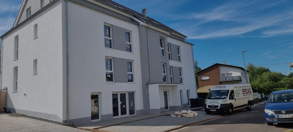Mehrfamilienhaus mit weißer Fassade und grauen Fensterbändern von der Straße aus.