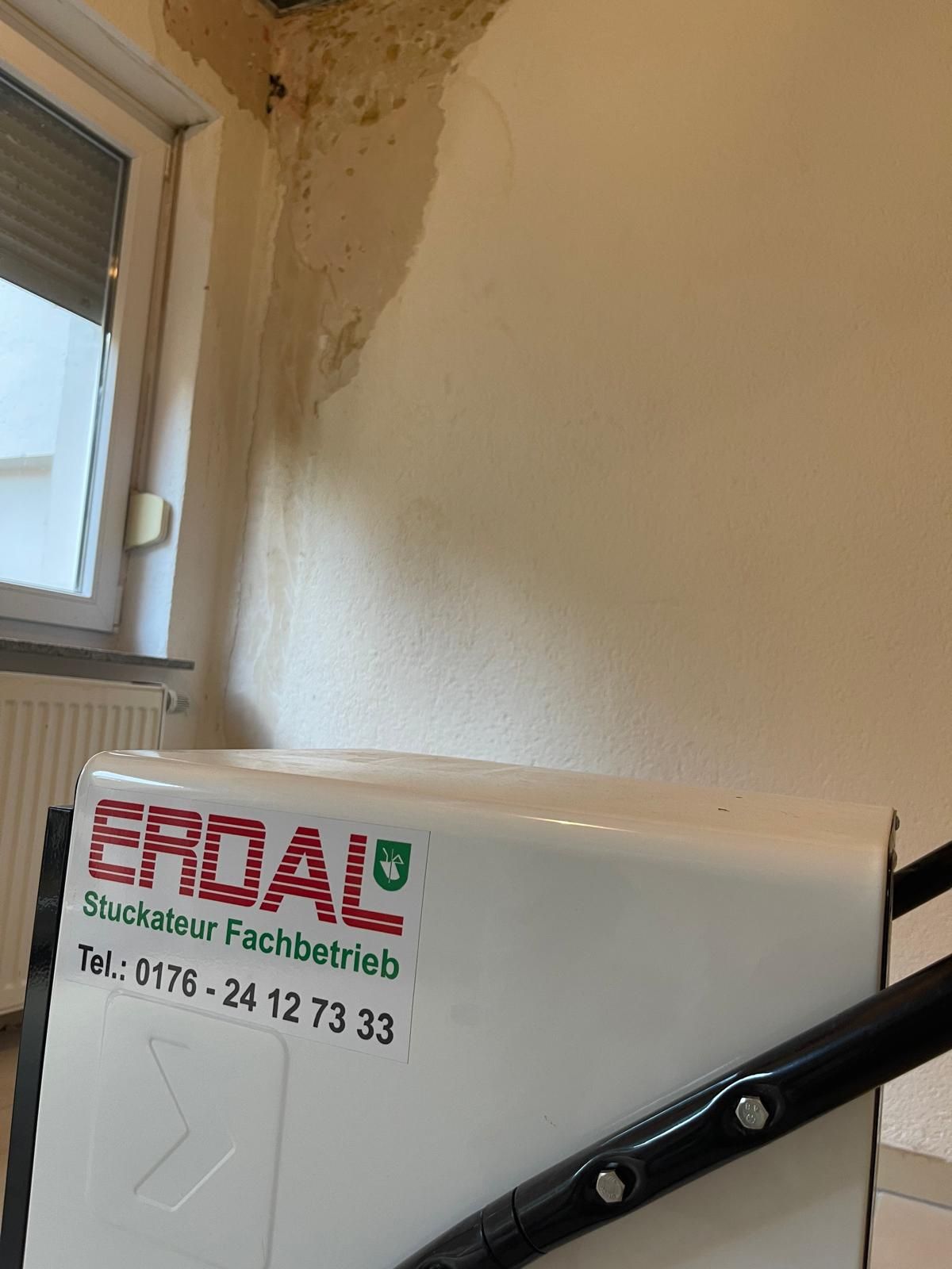 Bautrockner mit Erdal-Aufkleber vor einer Zimmerwand mit Wasserflecken unter der Decke.